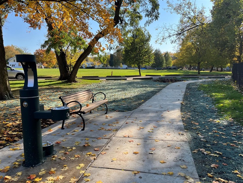 Paved path with a bench and drinking fountain with dog bowl.