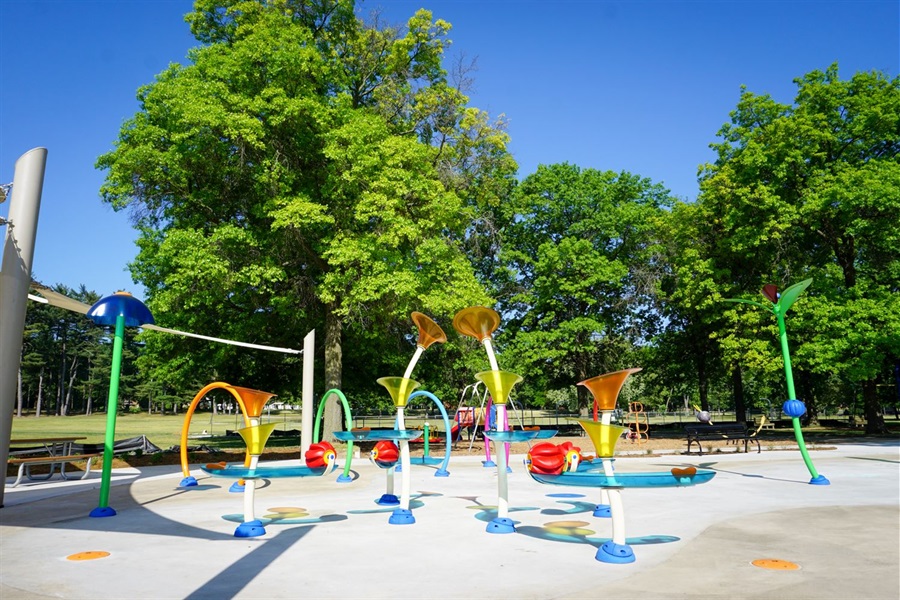 Image of a splash pad with brightly colored spray features, shade sails and picnic tables