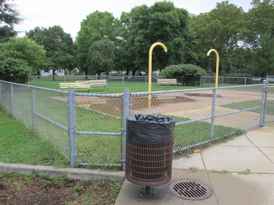 An outdated splash pad sits behind a chain link fence.