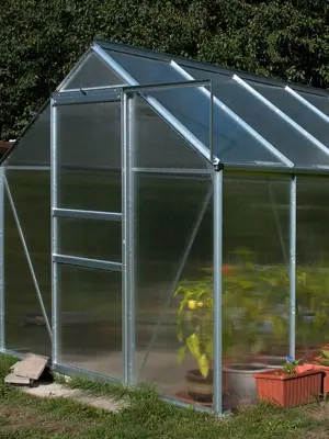 A small outdoor greenhouse constructed of translucent plastic siding and aluminum rails.