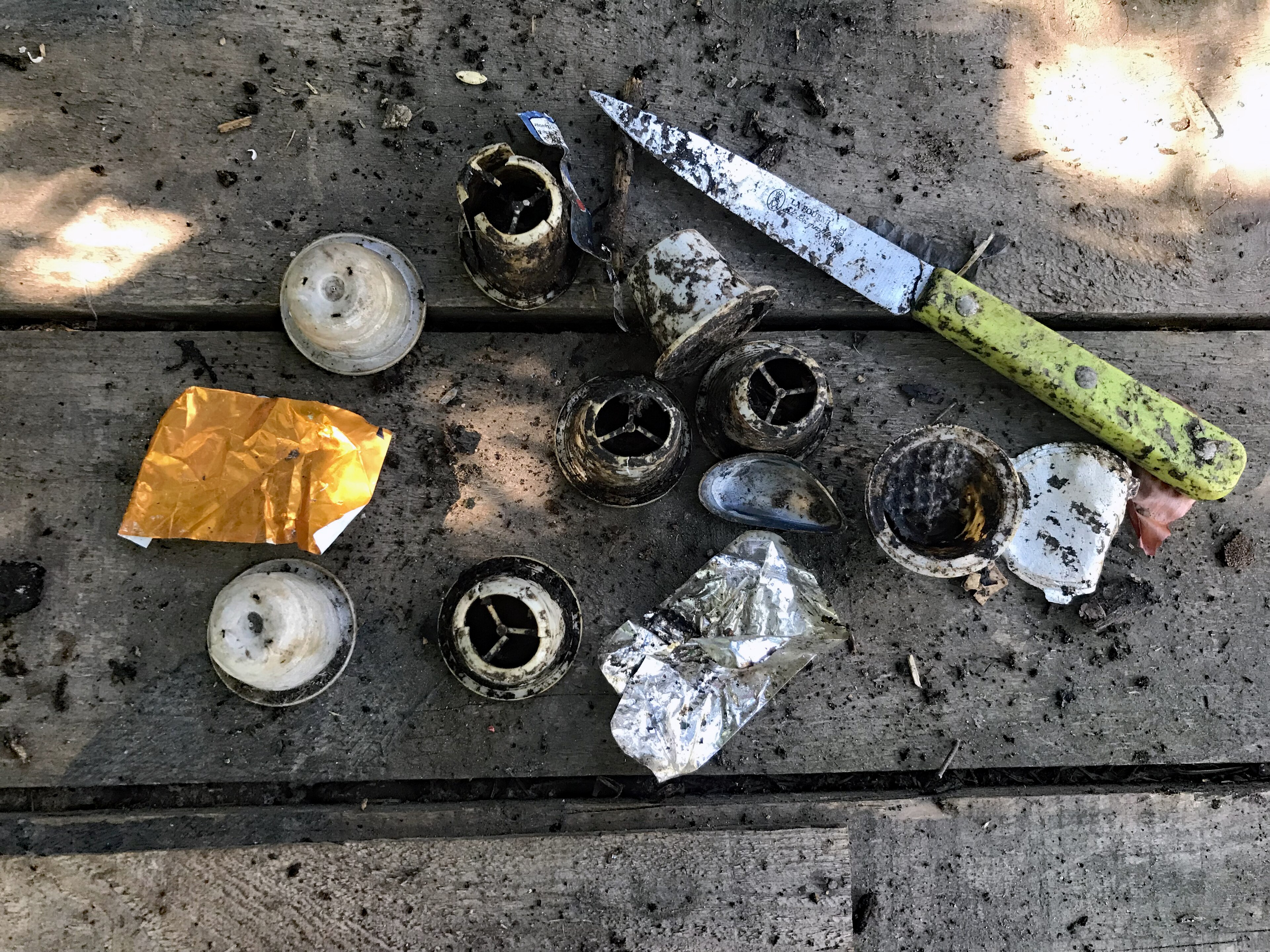 Items taken out a compost bin including a knife, plastic coffee filters, and foil wrappers.