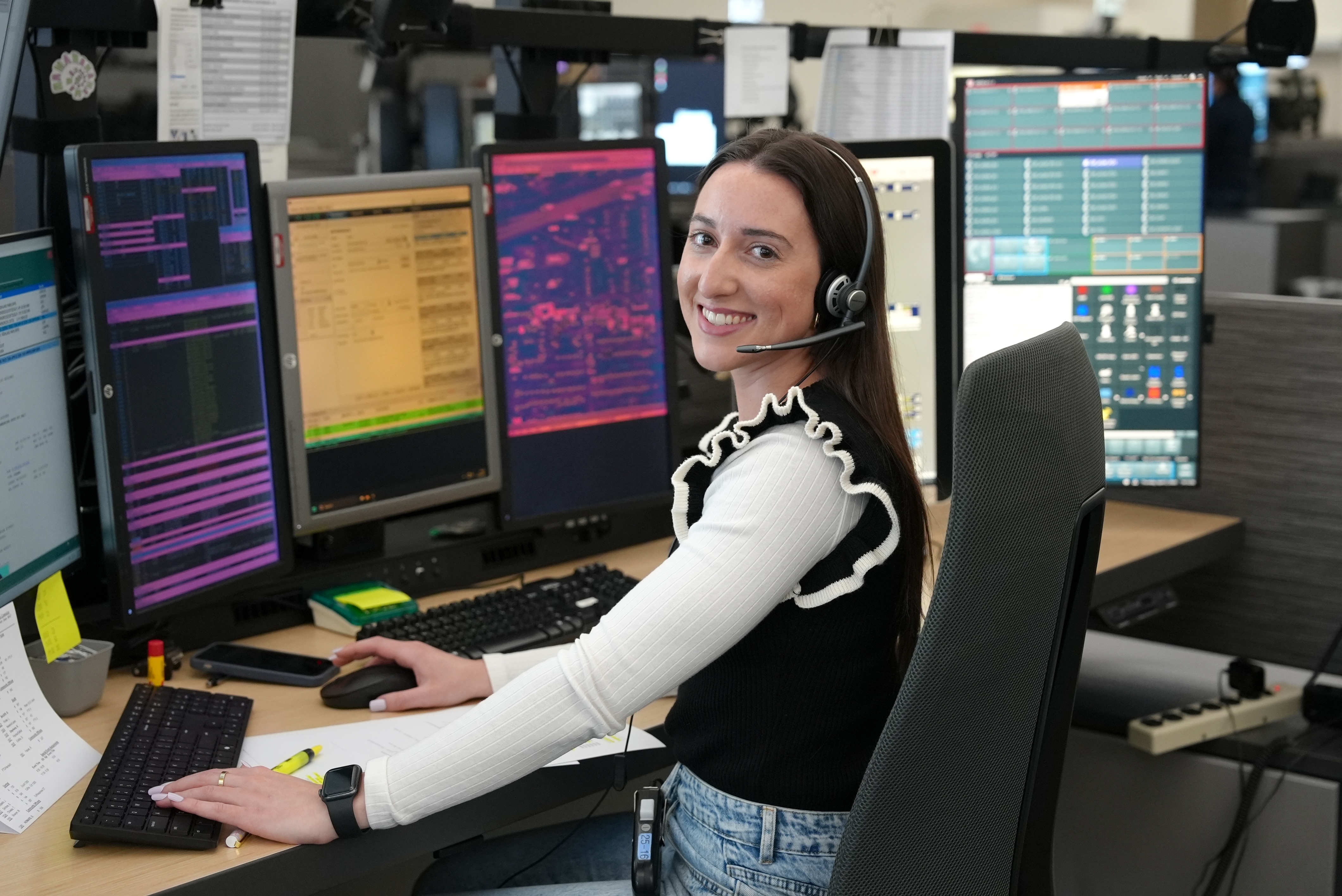 smiling emergency communications operator sitting at their computer with multiple screens monitoring the 9-1-1 call center