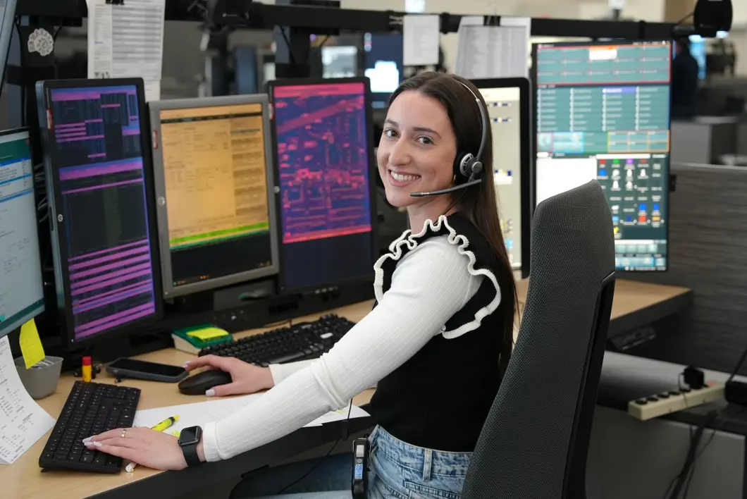 smiling emergency communications operator sitting at their computer with multiple screens monitoring the 9-1-1 call center