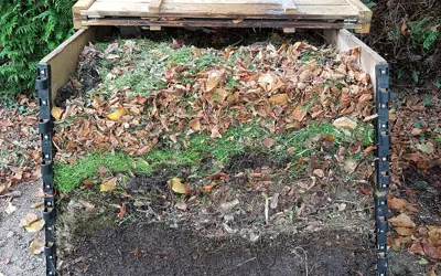 The side of an outdoor compost bin is removed to show alternating layers of brown and green materials.